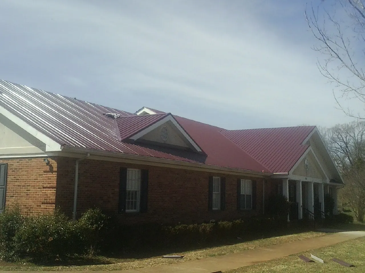 Red metal roof with gabled entries on a long brick building, from a Hail Damage Roof Repair job in New Riegel