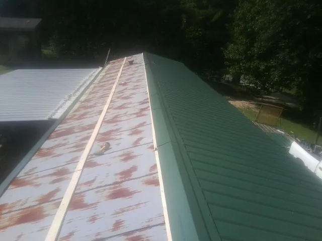 Old rusted panels beside newly installed green metal roofing — Wind Damage Roof Repair by Roofing Brothers in New Riegel