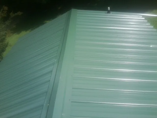 New green metal panels meeting at the ridge of a roof — Flat Roof Repair work by our crew in New Riegel
