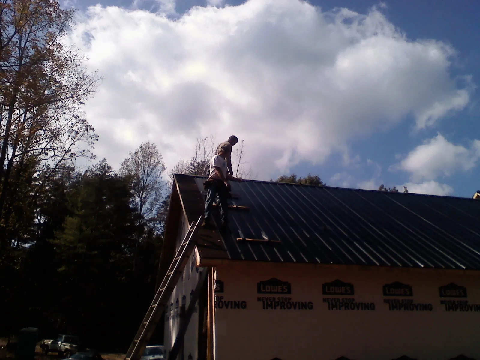 Roofer fastening dark metal panels high against a cloudy sky, from a Roof Inspection job in New Riegel