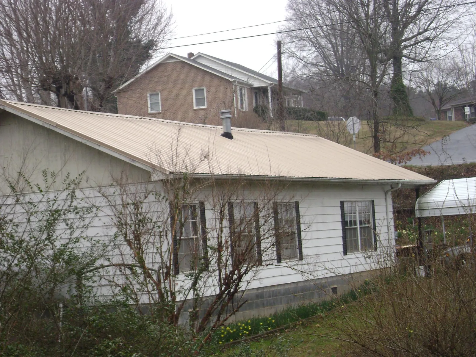 Tan metal roof on a white sided house set into a hillside — Commercial Roofing by Roofing Brothers in New Riegel