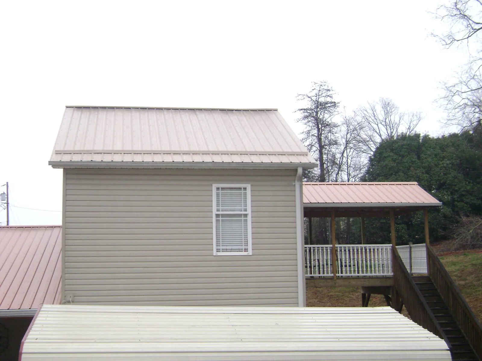 Tan metal roofs on a two story addition and attached porch, from a Roof Replacement job in New Riegel